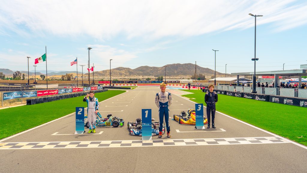 The top three finishers from COTF America Round 4 in the KA100 Junior division stand next to theirkarts on on the start finish line.